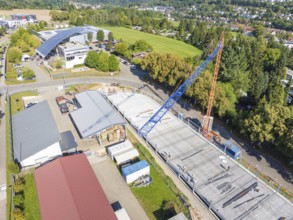 Construction site under blue sky with crane in urban environment and many trees, car park