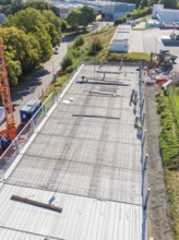 Workers on construction site with crane in sunny weather, surrounded by roads and fences, car park