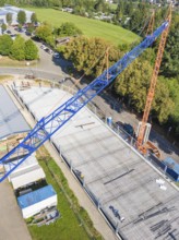 View from above of a construction site with a blue crane and construction workers, surrounded by