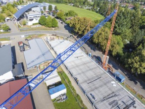 Large crane over construction site during building work in green surroundings with roads, car park
