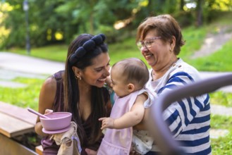 Grandmother holding her granddaughter while mother is feeding her in a park, enjoying family time