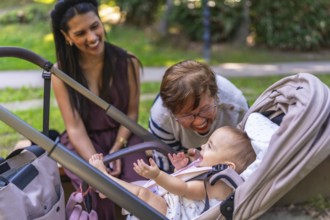 Grandmother and mother taking care of a baby girl in a stroller, playing and laughing together in a