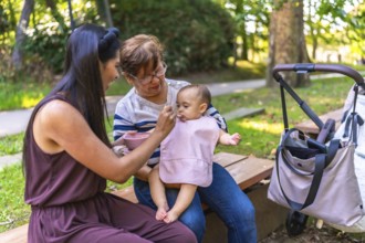 Latin family enjoying a sunny day outdoors, with grandmother and mother lovingly feeding a baby