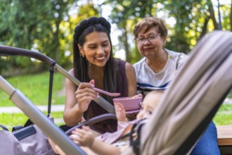 Mother feeding her baby girl with grandmother watching, enjoying family time together at the park