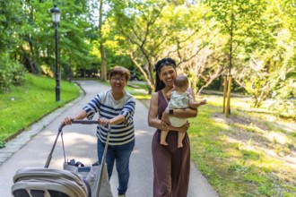 Happy latin family walking in a park, grandmother pushing a stroller and mother holding her baby
