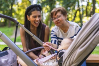 Grandmother feeds baby girl sitting in stroller, while mother watches, enjoying family time