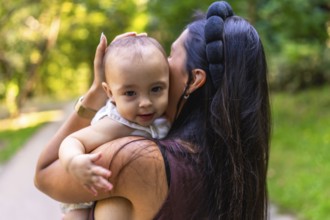 Mother cuddling her baby girl while strolling through a park, savoring a sunny day filled with