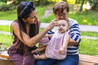 Grandmother holding baby girl while mother feeding her in the park, cherishing moments of family