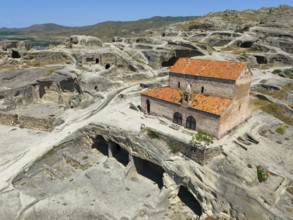 Fascinating ruins of Uplistsikhe with orange tiled roofs in the middle of a rocky landscape, aerial