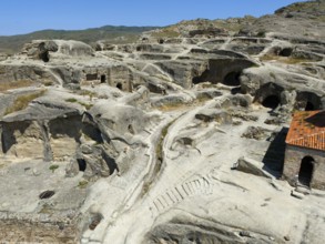 Ancient cave town with weathered sandstone structures and old paths under a blue sky, aerial view,