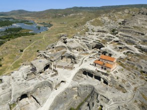Ruins of the ancient cave city of Uplistsikhe overlooking a wide river and hilly landscape, aerial