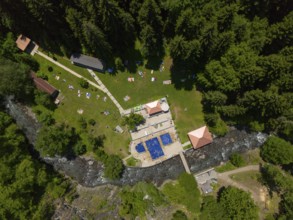Aerial view of a forest area with swimming pool, river and surrounding buildings, surrounded by