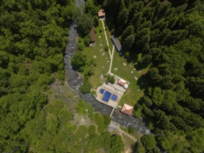 Aerial view of a forest area with swimming pool and river, surrounded by dense trees and buildings,