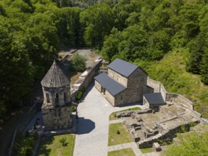 Historic monastery complex embedded in a forest, with ruins and stone structures, aerial view,