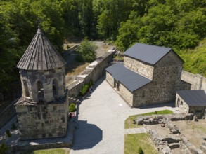 Aerial view of a monastery with stone buildings, surrounded by forest and sky in summer light,