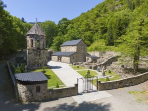 Historic monastery surrounded by lush greenery and blue sky, surrounded by ruins and vegetation,