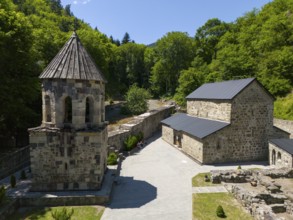 Stone chapel with adjoining buildings in a forest landscape under a clear blue sky, aerial view,