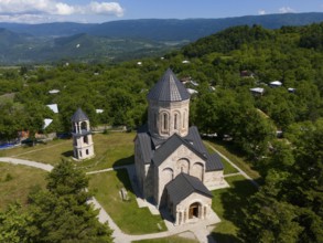 Traditional church surrounded by green landscape and hilly surroundings under blue sky, aerial