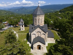 Historic church in a green mountain landscape under a blue sky with clouds, aerial view,