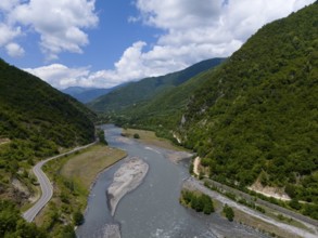 A river flows through a mountainous valley along a winding country road, aerial view,