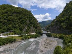A river meanders through a wooded valley, with a bridge connecting the two banks, aerial view,