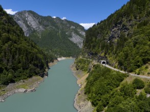 A turquoise-coloured river flows through a wooded valley with mountains and a tunnel in the