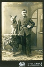 Young man with simple uniform and dog, studio photograph, around 1910