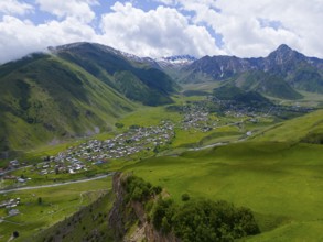 Panoramic view of green valley with village and mountains under a cloudy sky, aerial view, view