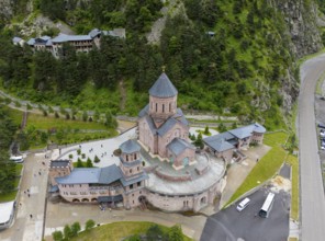 Large red brick church embedded in a wooded mountain landscape under a slightly cloudy sky, aerial