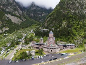 A large red brick church lies picturesquely in a mountainous valley under clouds, aerial view,