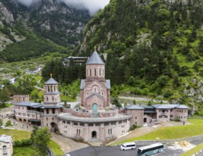 Impressive red brick church surrounded by forested mountains under a cloudy sky, aerial view,