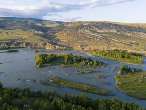 A picturesque river landscape with green islands and surrounding hills under a blue sky, aerial