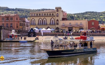 Sardinia, boats in the river Temo and houses on the promenade, guests at the restaurants with