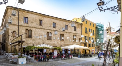 Sardinia, tourist tour group in the old town with sandstone-coloured palazzi, birdcage from house