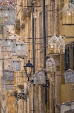 Sardinia, birdcage with light bulbs on power lines between houses above the alleyway, old town,