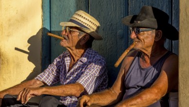 Two old Cubans smoking cigars and sitting on a staircase in the warm light of the sunset, Trinidad,