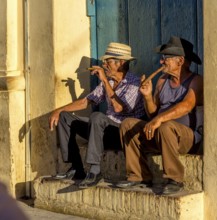 Two old Cubans smoking cigars and sitting on a staircase in the warm light of the sunset, Trinidad,