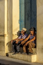 Two old Cubans smoking cigars and sitting on a staircase in the warm light of the sunset, Trinidad,