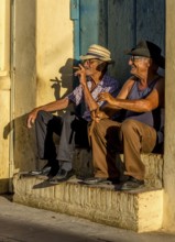 Two old Cubans smoking cigars and sitting on a staircase in the warm light of the sunset, Trinidad,