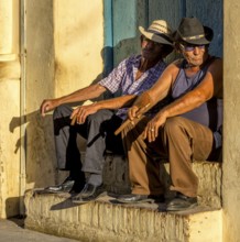Two old Cubans smoking cigars and sitting on a staircase in the warm light of the sunset, Trinidad,