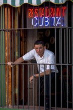 Waiter waiting for customers behind the window bars of the Cubita Restaurant, Trinidad, Cuba,