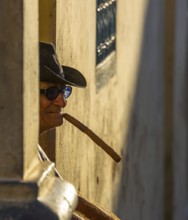 An old Cuban smokes a cigar and sits on a staircase in the warm light of the sunset, Trinidad,