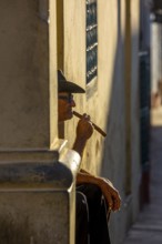 An old Cuban smokes a cigar and sits on a staircase in the warm light of the sunset, Trinidad,