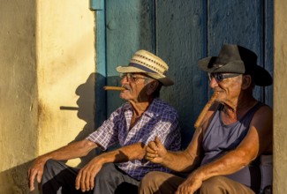 An old Cuban smokes a cigar and sits on a staircase in the warm light of the sunset, Trinidad,