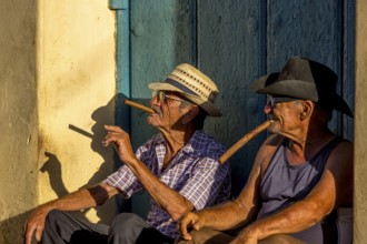 Two old Cubans smoking cigars and sitting on a staircase in the warm light of the sunset, Trinidad,