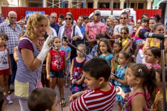 A young girl with a microphone plays clown and entertains children, Streetlife in the city centre