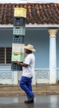Cuban man with hat carrying and balancing crates of drinks across a street in Vinales, Viñales,