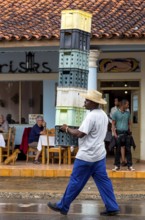 Cuban man with hat carrying and balancing crates of drinks across a street in Vinales, Viñales,