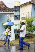Cuban man with hat carrying and balancing crates of drinks across a street in Vinales, Viñales,