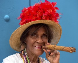 Old Cuban woman smokes a Cuban cigar on the street and posts with her cat for the tourists, La
